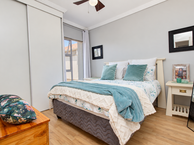 A well-maintained bedroom featuring laminate flooring, crown molding, a ceiling fan, and a built-in wardrobe with sliding doors.