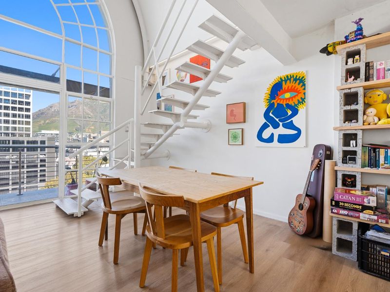 Bright living area featuring a striking arched window, modern metal staircase, and direct access to a balcony with urban and mountain views.