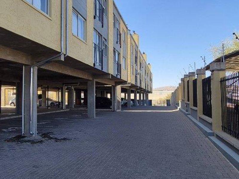 Exterior view of the apartment complex featuring a paved driveway, covered parking area, and secure perimeter fencing.