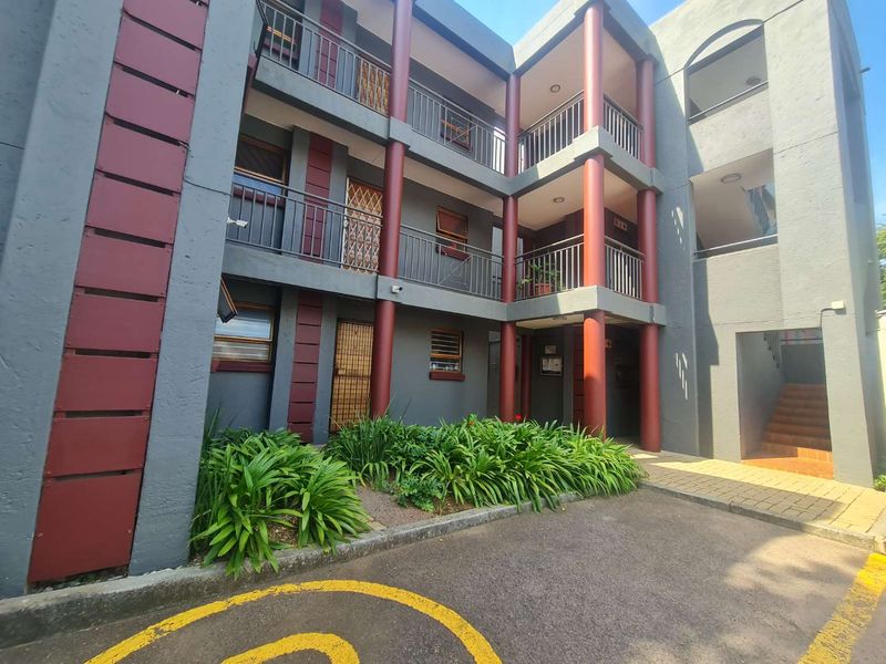 Exterior view of a multi-story apartment building featuring metal security gates, balcony railings, and a landscaped garden area at the entrance.