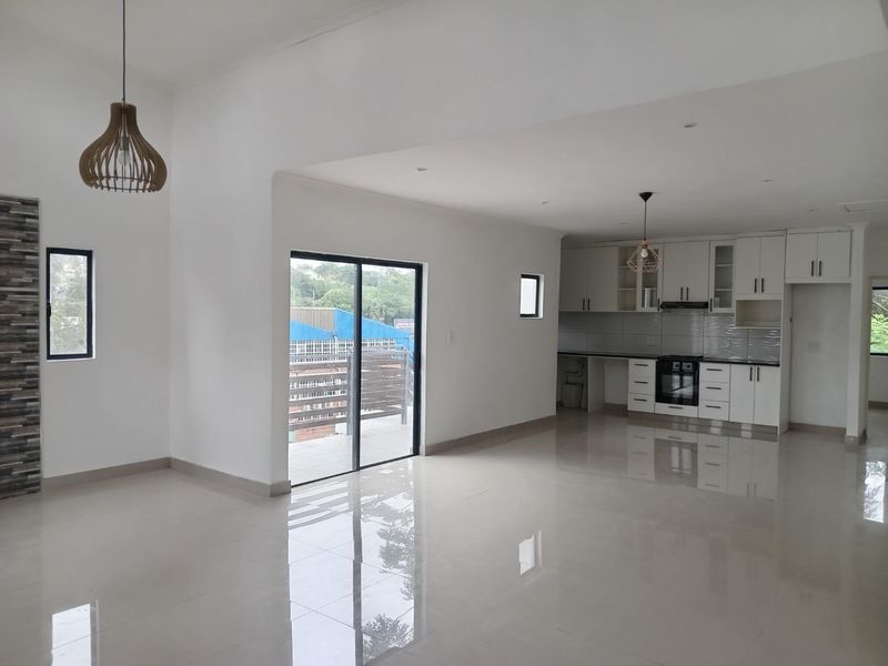 Spacious open-plan living and kitchen area featuring polished tile floors, modern white cabinetry, integrated appliances, and direct access to an outdoor balcony.