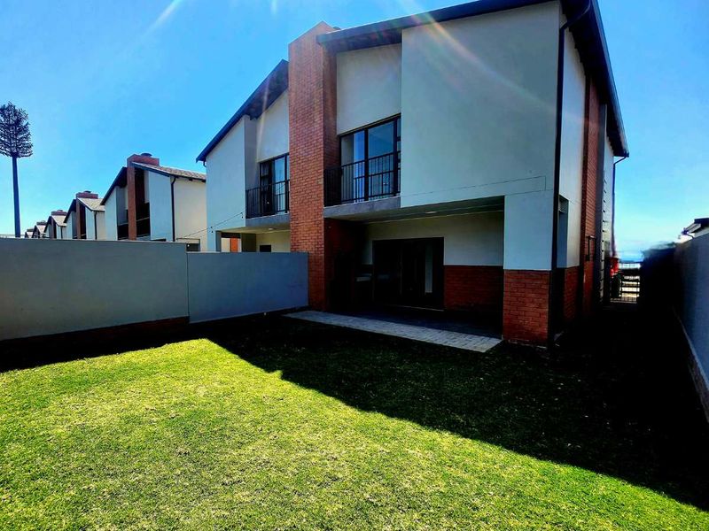 Rear view of the townhouse featuring a private garden, paved patio area, and upper-level balcony with sliding glass doors.