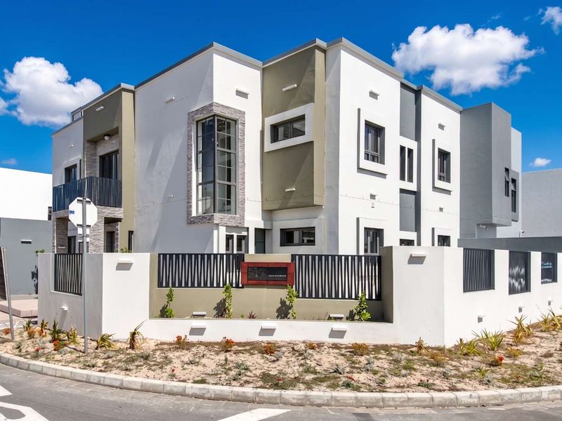 A modern multi-story residential building featuring a contemporary facade with stone accents, metal fencing, and a balcony, situated on a corner lot.