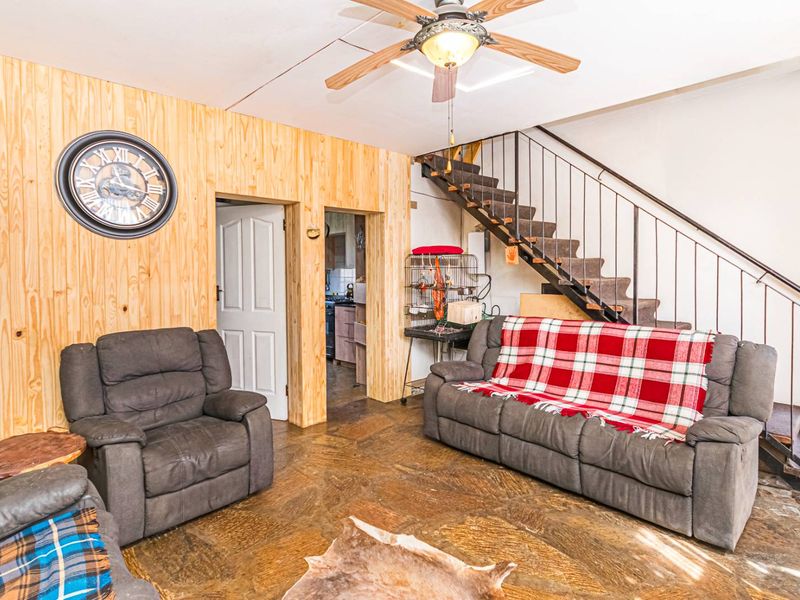Living room featuring stone flooring, wood-paneled walls, and an open staircase with a metal handrail, providing a rustic aesthetic.