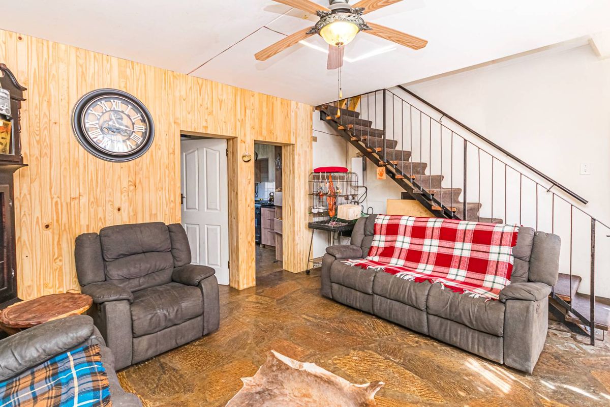 Living room featuring stone flooring, wood-paneled walls, and an open staircase with a metal handrail, providing a rustic aesthetic.