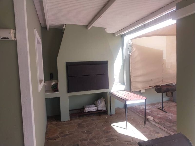 Covered outdoor patio area featuring a built-in braai, stone flooring, and a shade sail, providing a functional space for outdoor entertaining.