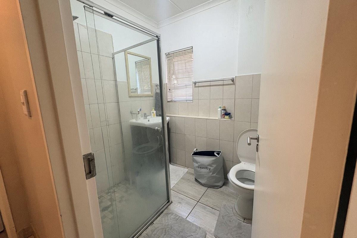 A functional bathroom featuring a glass-enclosed shower, pedestal basin, and toilet, finished with neutral wall and floor tiles.
