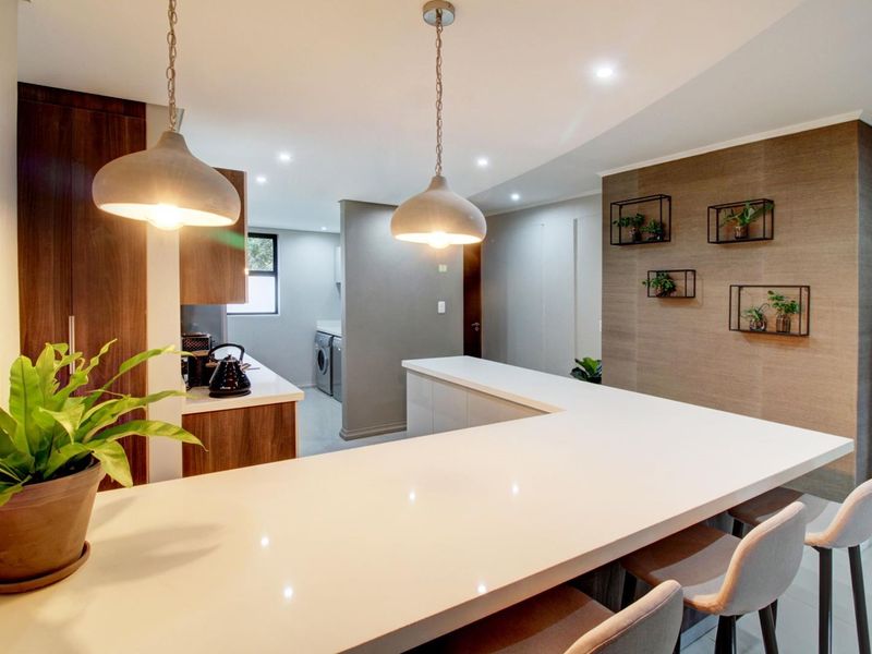 Modern open-plan kitchen featuring a large quartz breakfast bar, sleek built-in cabinetry, and stylish pendant lighting, seamlessly flowing into the adjacent utility area.