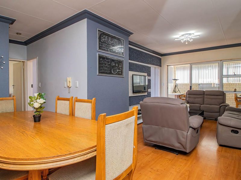 Open-plan living and dining area featuring laminate flooring, crown molding, and sliding glass doors leading to an enclosed balcony.