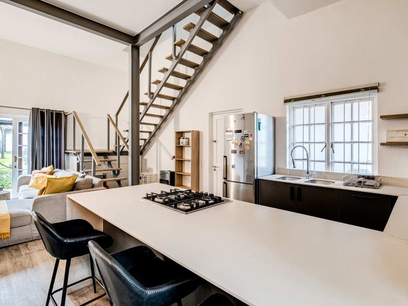 Modern open-plan living area featuring a kitchen island with gas hob, double sink, and a striking industrial-style staircase leading to an upper level.