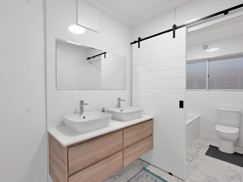 Modern bathroom featuring a double vanity with vessel sinks, a sliding barn door, and a separate bathtub and toilet area with tiled finishes.