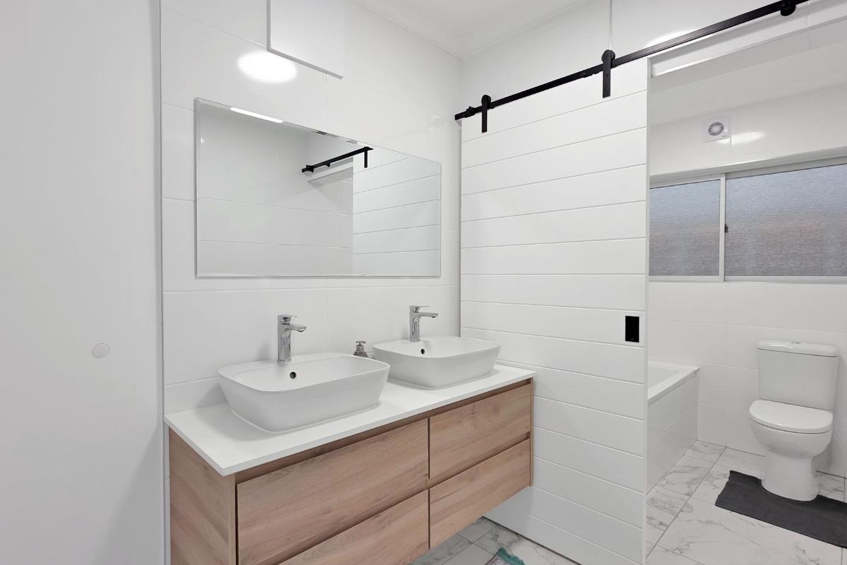 Modern bathroom featuring a double vanity with vessel sinks, a sliding barn door, and a separate bathtub and toilet area with tiled finishes.