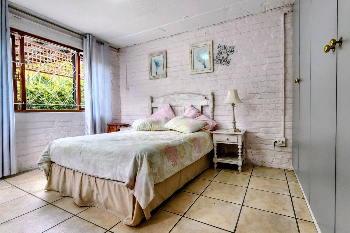 A bedroom featuring painted brick walls, tiled flooring, and built-in cupboards, with natural light provided by a window with security bars.