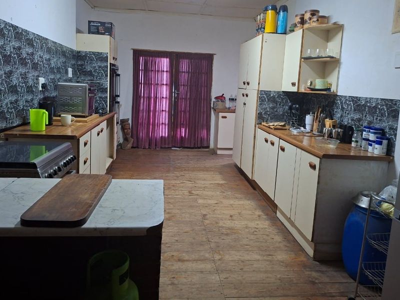 A dated kitchen featuring timber flooring, laminate countertops, and built-in cabinetry, with direct access to the outdoors through double glass doors.