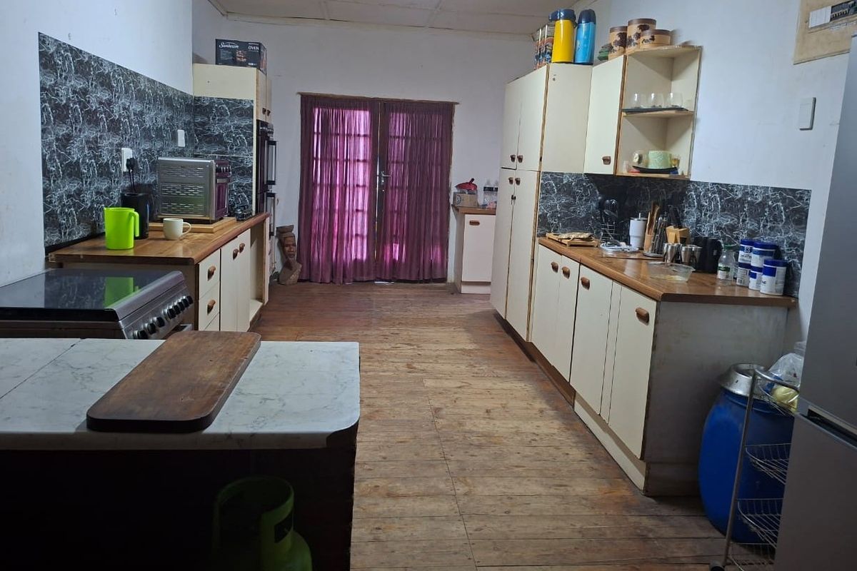A dated kitchen featuring timber flooring, laminate countertops, and built-in cabinetry, with direct access to the outdoors through double glass doors.