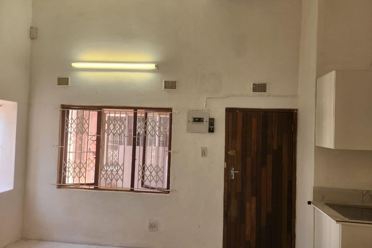 An open-plan living and kitchen area featuring tiled floors, security gates on windows, and basic cabinetry, requiring cosmetic updates to improve the interior finish.