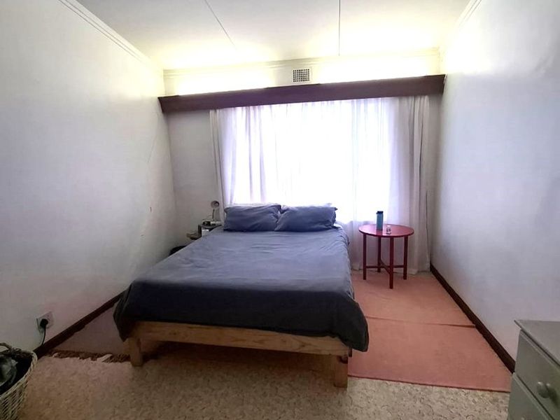 A bedroom featuring a large window with curtain rail, coving, and an air vent. The room requires cosmetic updates to the walls and flooring.