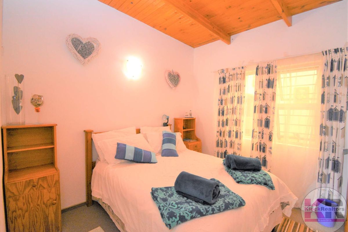 A cozy bedroom featuring a vaulted timber-beamed ceiling and a window with security bars, providing a warm and rustic atmosphere.