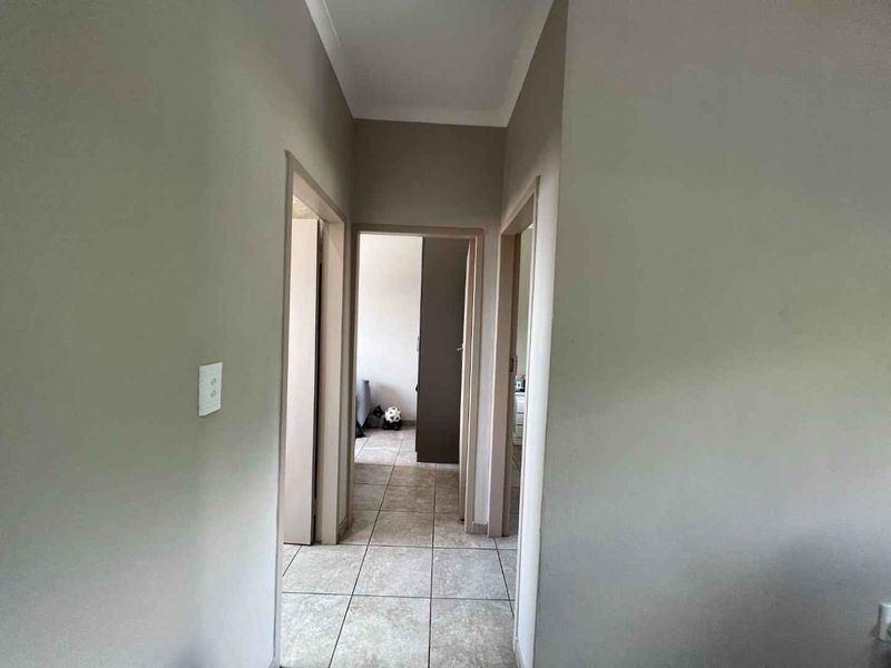 A neutral-toned hallway featuring tiled flooring and connecting multiple rooms within the apartment.