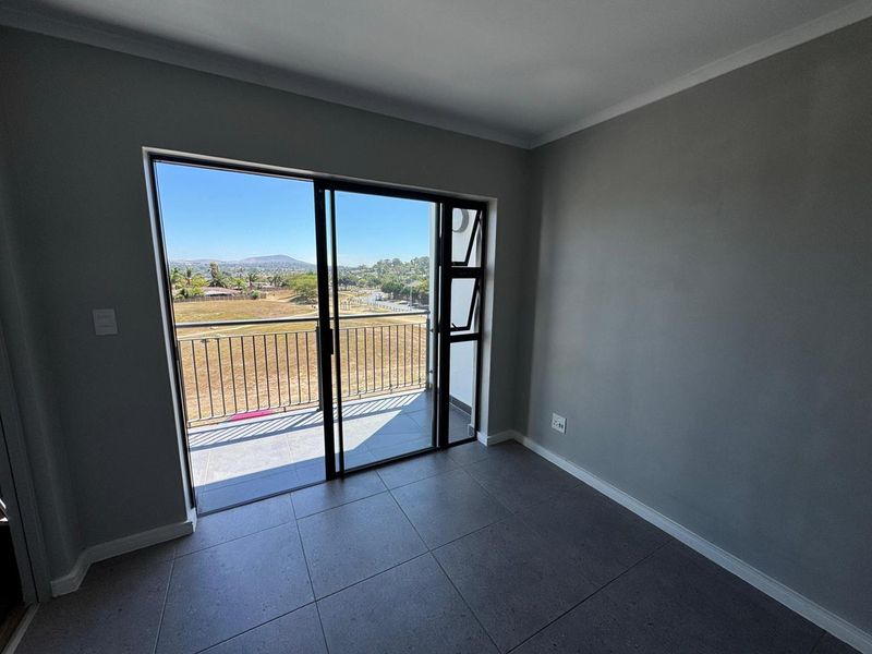 An empty bedroom featuring modern grey floor tiles, neutral walls, and a sliding glass door providing access to a balcony with scenic views.
