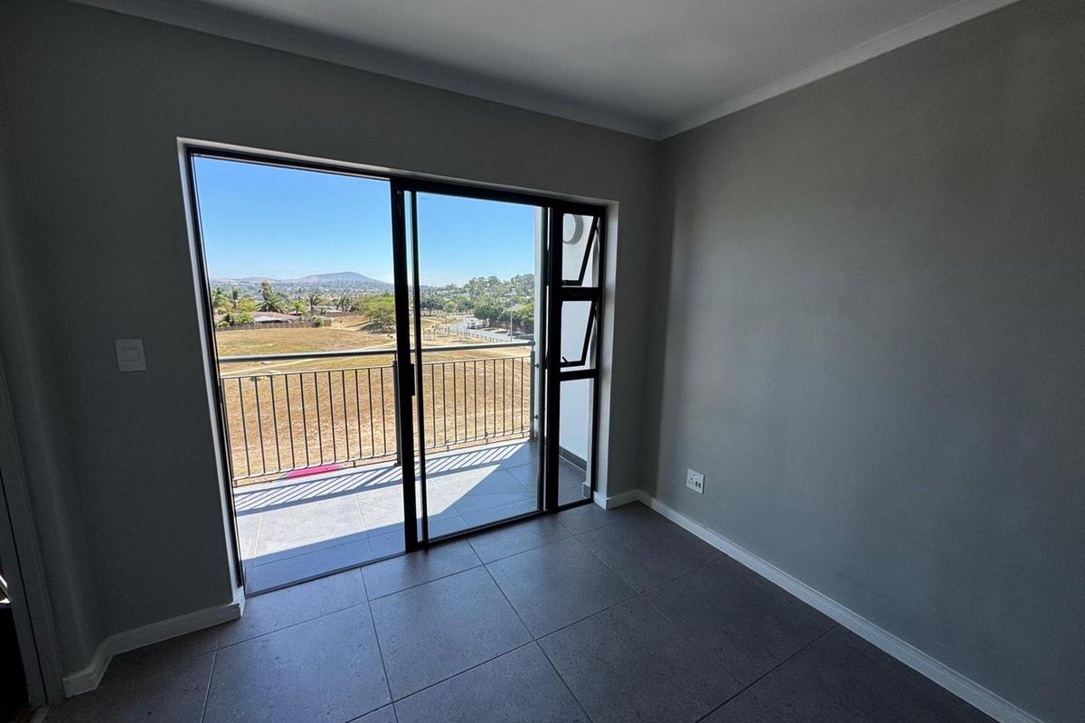 An empty bedroom featuring modern grey floor tiles, neutral walls, and a sliding glass door providing access to a balcony with scenic views.