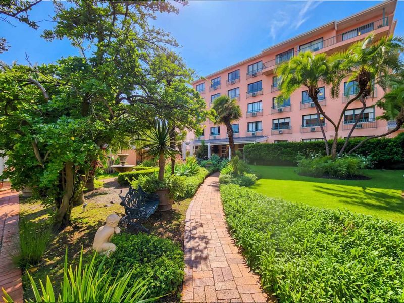A well-maintained rear garden featuring a brick paved pathway, lush landscaping, and a view of the multi-story apartment building facade with balconies.