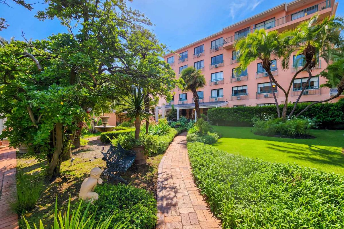 A well-maintained rear garden featuring a brick paved pathway, lush landscaping, and a view of the multi-story apartment building facade with balconies.