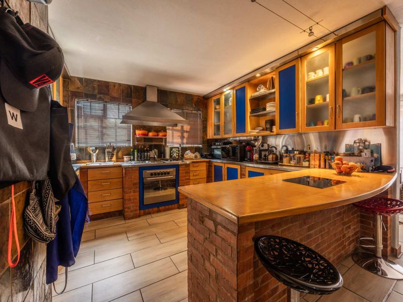 A rustic-style kitchen featuring brick accents, wooden cabinetry with blue panels, a breakfast bar, and integrated appliances with slate tile backsplash.