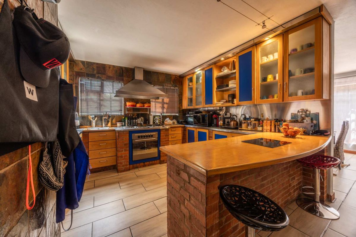A rustic-style kitchen featuring brick accents, wooden cabinetry with blue panels, a breakfast bar, and integrated appliances with slate tile backsplash.