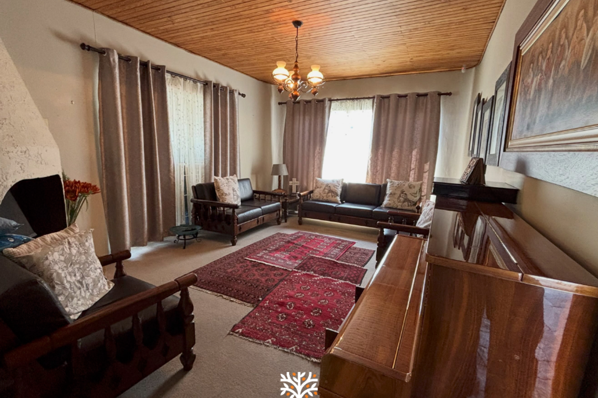 A spacious living room featuring a warm timber tongue and groove ceiling, carpeted flooring, and a traditional built-in fireplace.