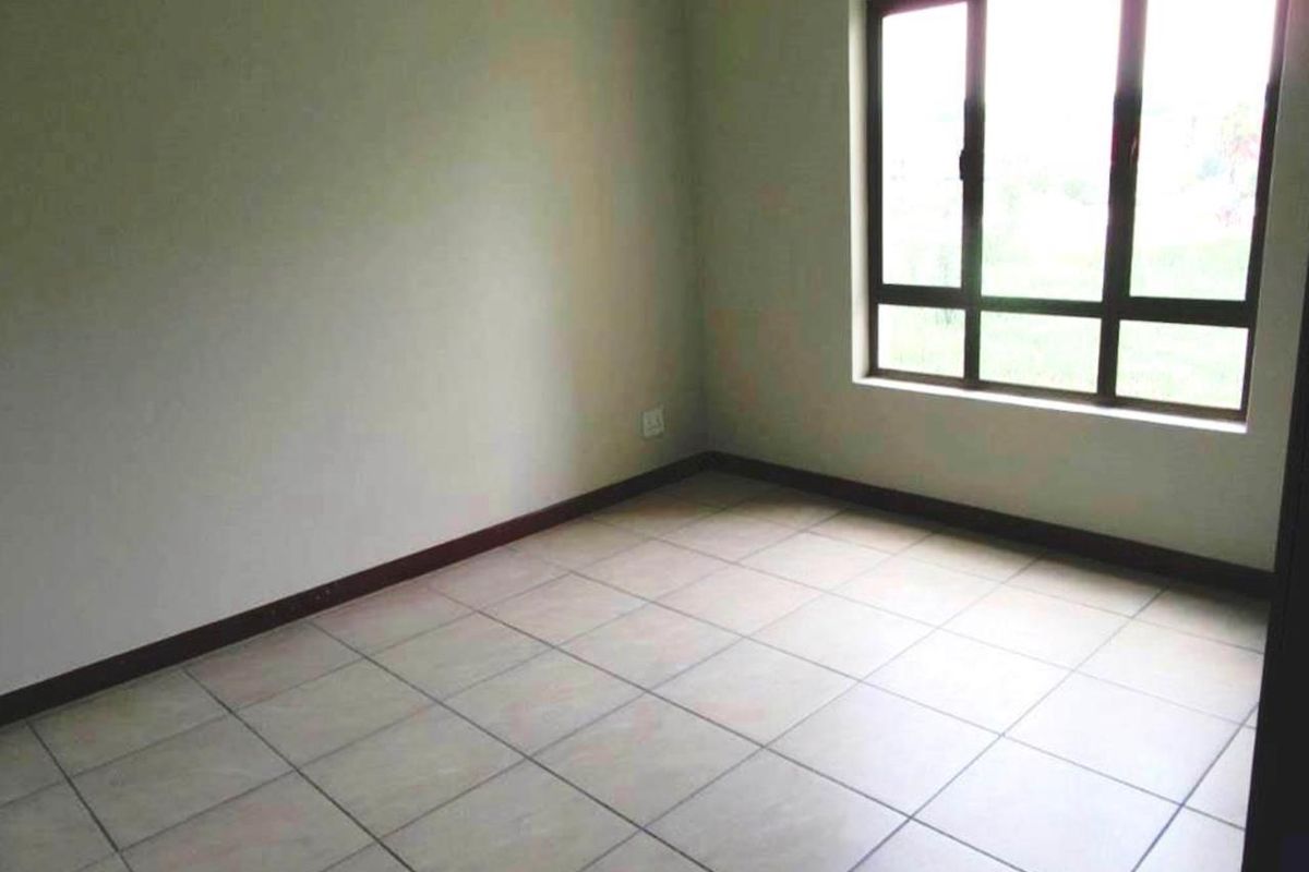 A vacant bedroom featuring neutral tiled flooring, clean walls, and a large aluminium-framed window providing natural light.