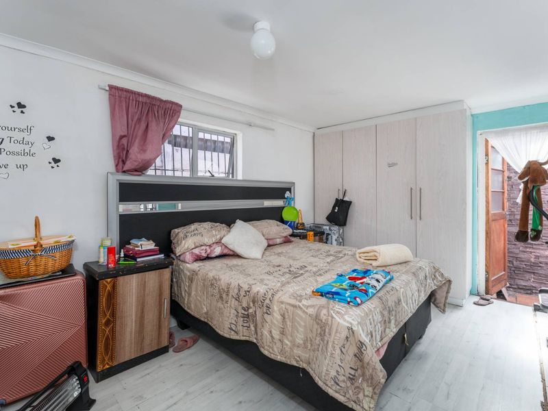 A functional bedroom featuring built-in cupboards, laminate flooring, and a window with security bars, offering a practical living space.