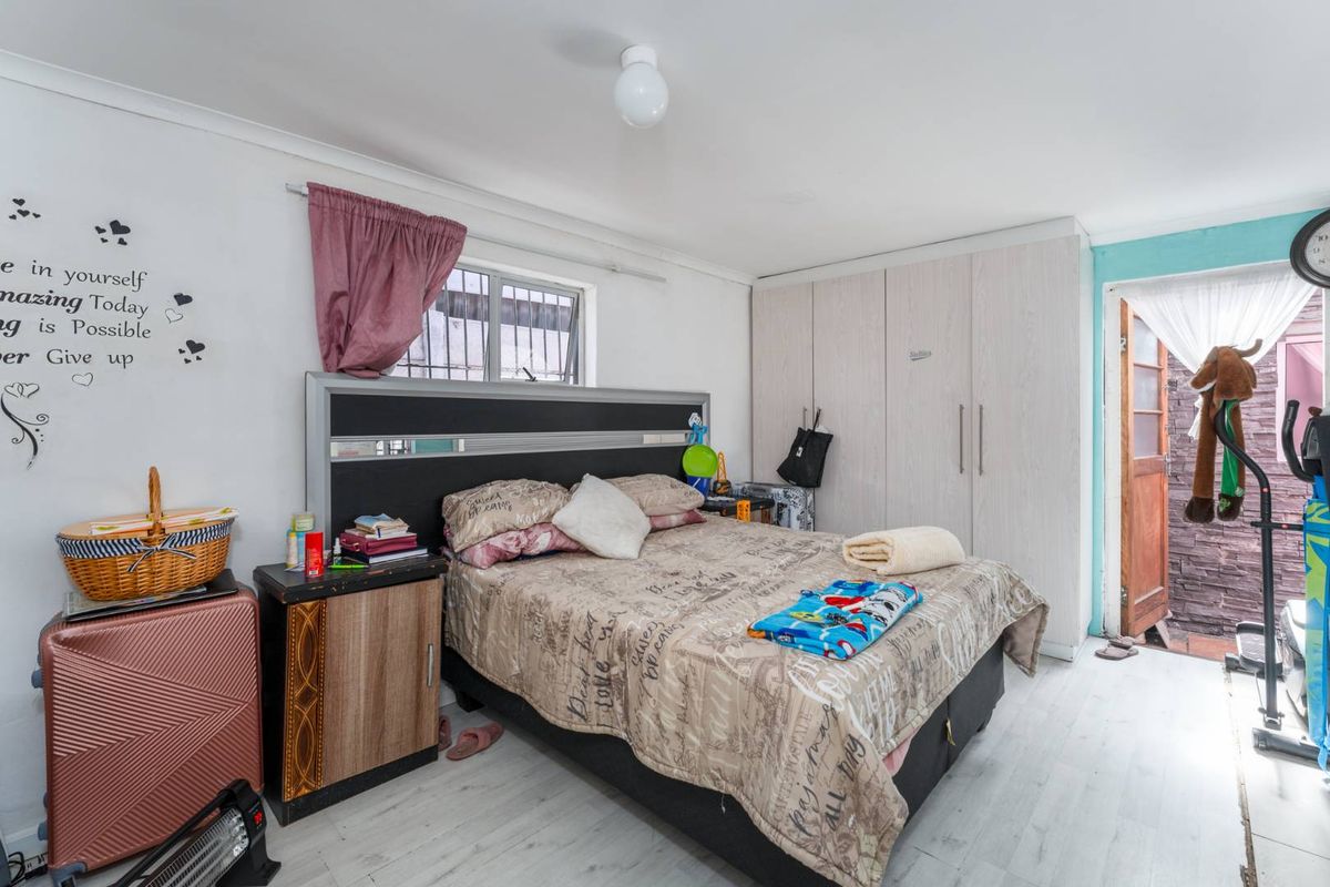 A functional bedroom featuring built-in cupboards, laminate flooring, and a window with security bars, offering a practical living space.