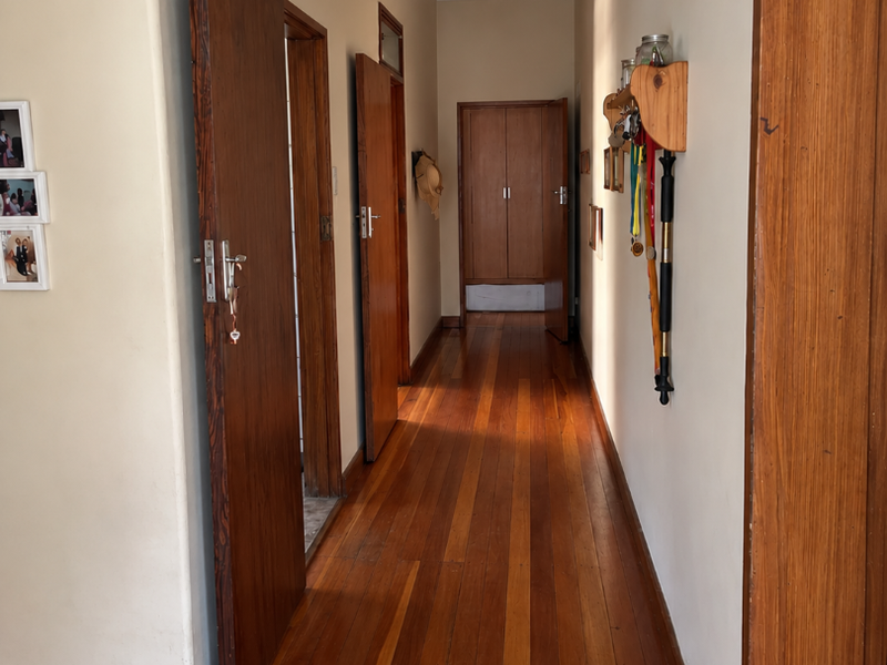 A well-maintained hallway featuring polished hardwood flooring, timber door frames, and a built-in storage cupboard at the end of the passage.