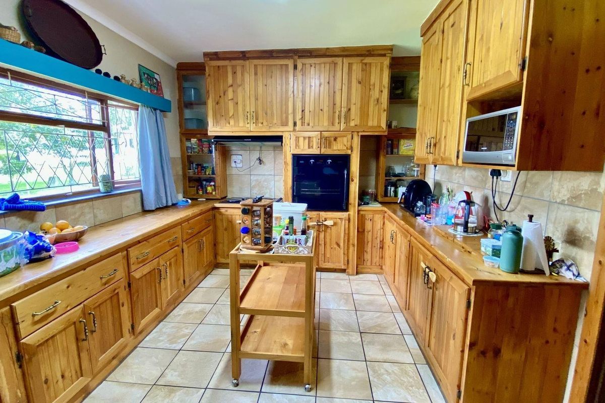 A traditional kitchen featuring extensive wooden cabinetry, tiled flooring, built-in oven, and ample counter space with a large window providing natural light.