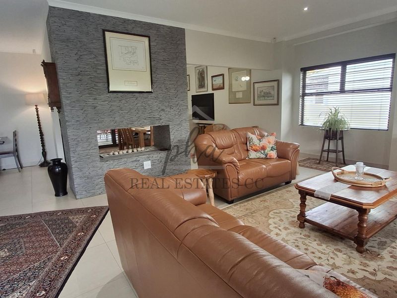 Spacious living room featuring a prominent stone-clad fireplace, neutral tiled flooring, and ample natural light through large windows.
