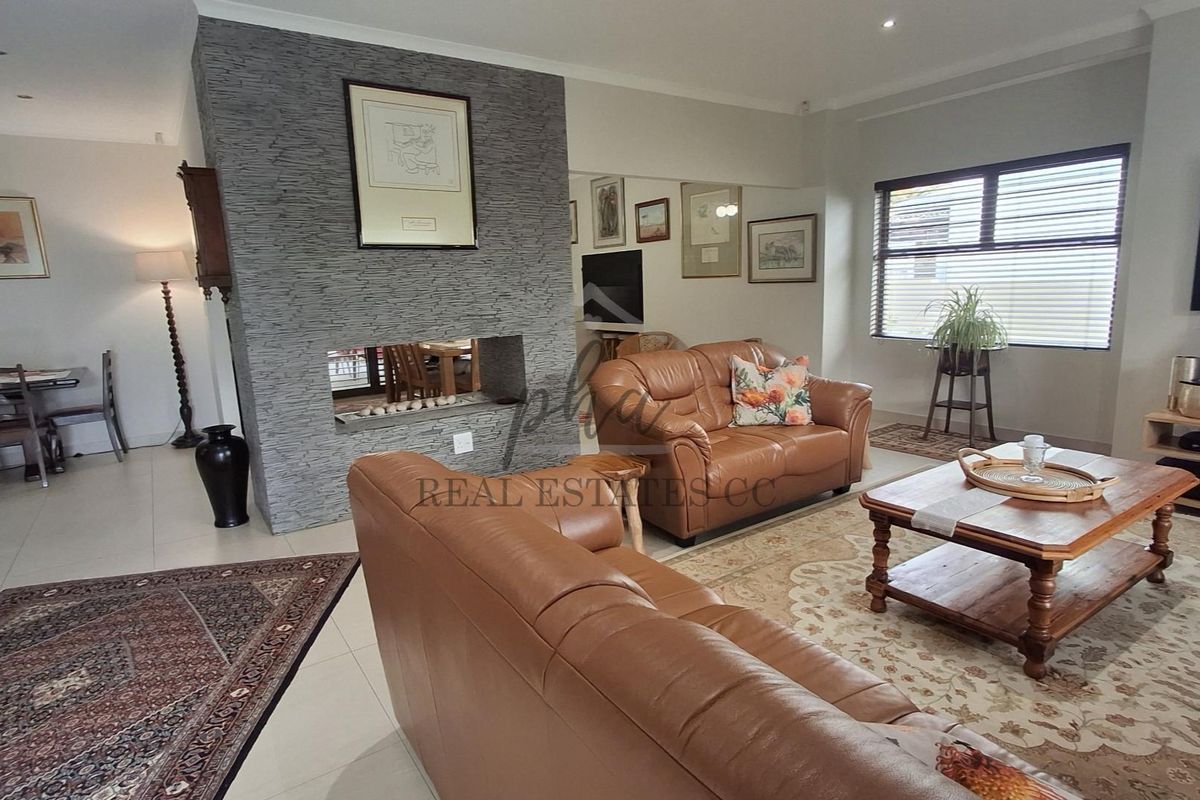 Spacious living room featuring a prominent stone-clad fireplace, neutral tiled flooring, and ample natural light through large windows.