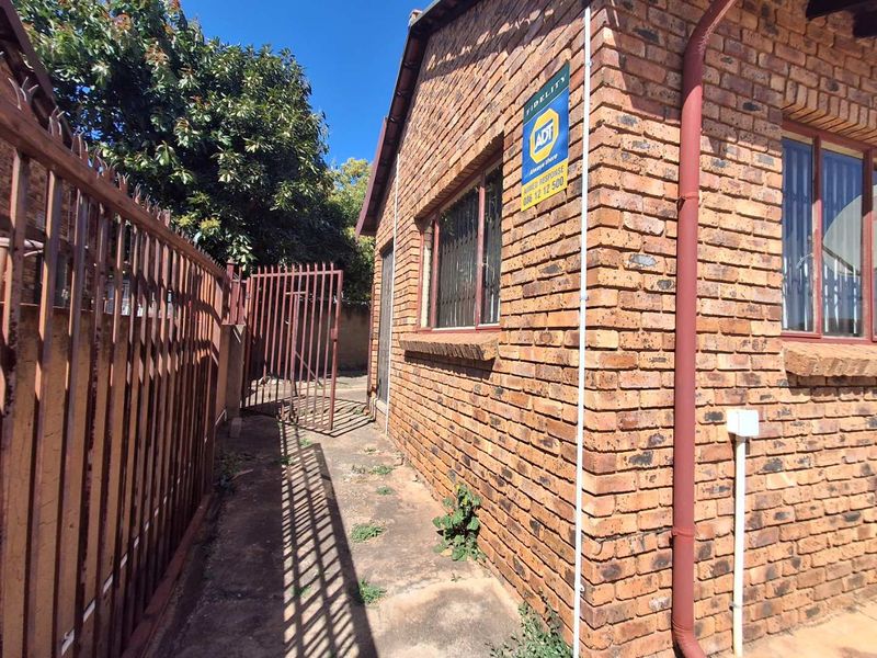 A side view of the face brick exterior featuring security bars on windows, a metal security gate, and an installed alarm system.