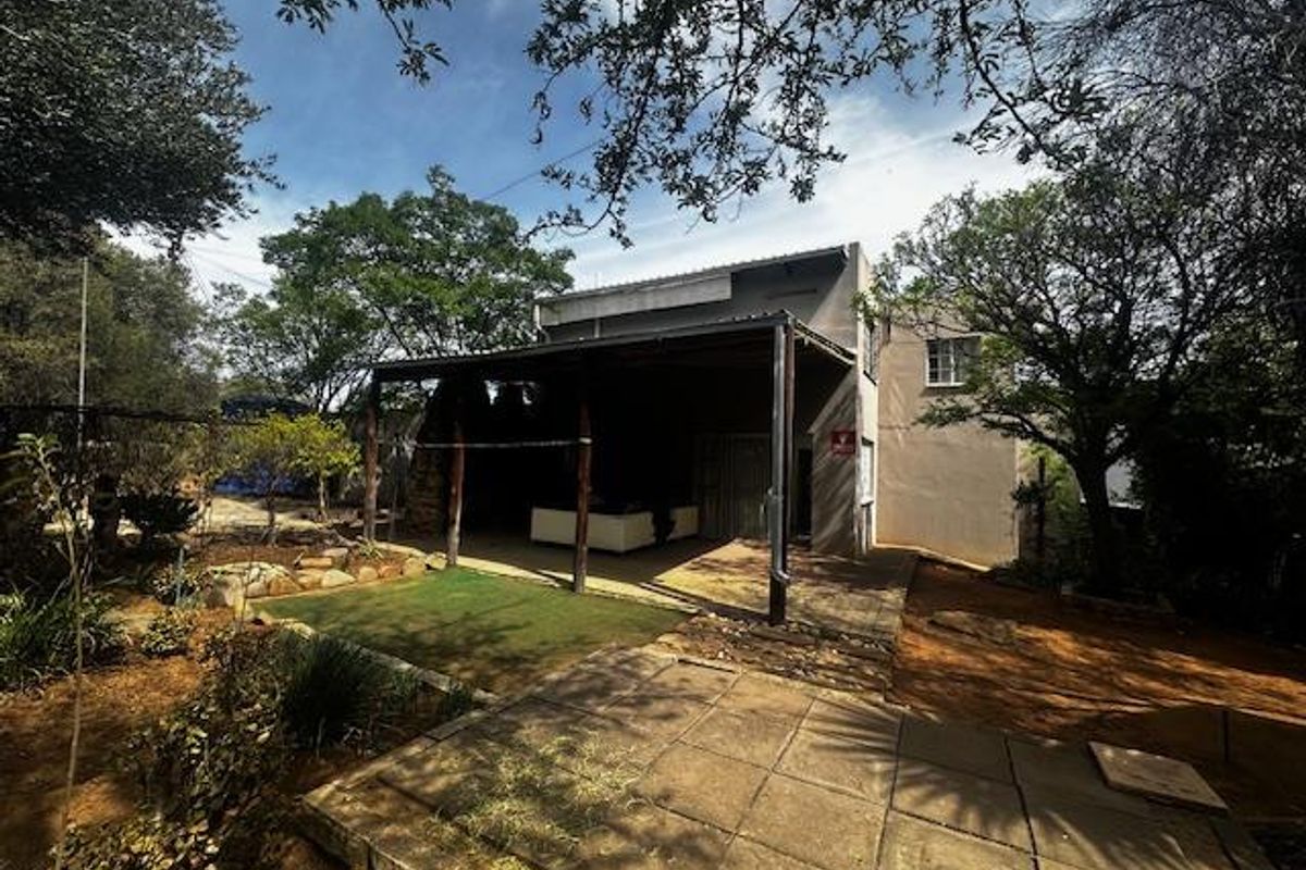 Rear view of the property featuring a covered patio area, paved outdoor space, and established garden surroundings.