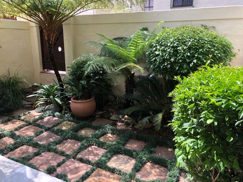 A well-maintained private garden area featuring stone pavers, lush established greenery, and a secure boundary wall with a timber access gate.