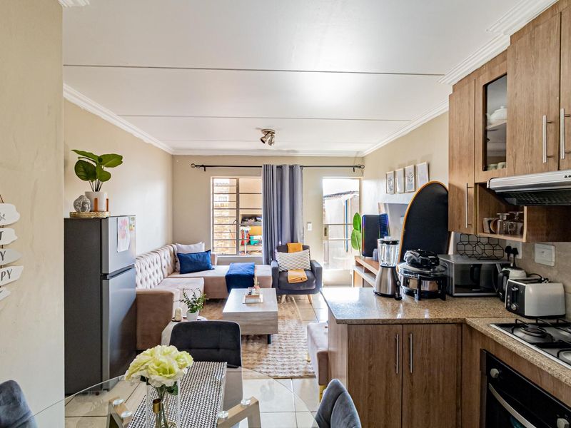 Open-plan living area featuring a functional kitchen with granite countertops, gas hob, and tiled flooring, seamlessly flowing into the lounge with outdoor access.