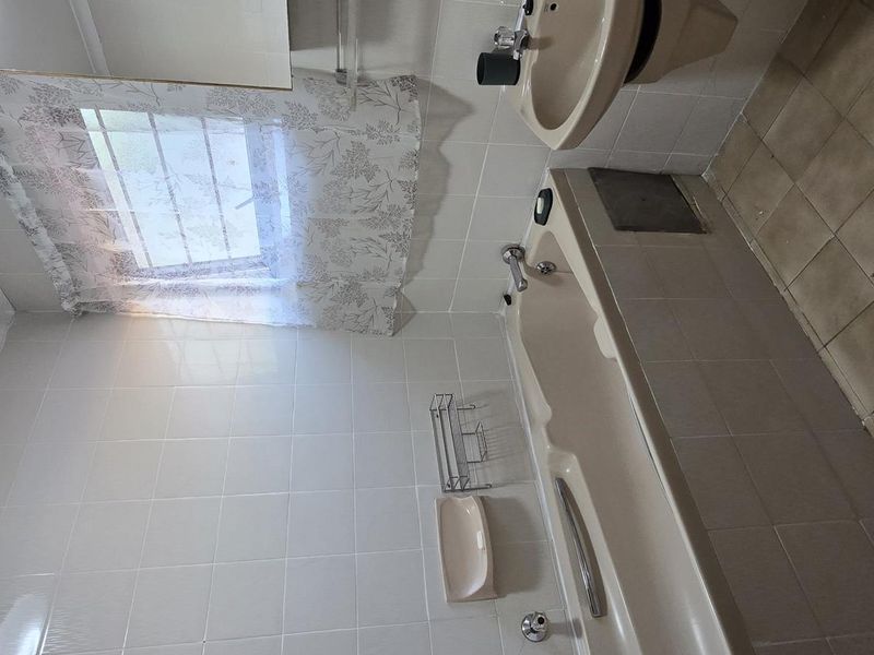 A functional bathroom featuring a bathtub, wall-mounted basin, and neutral tiled finishes, offering a blank canvas for modern renovation.