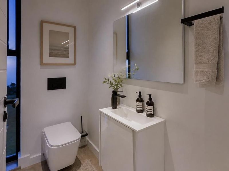 A modern, compact guest bathroom featuring a wall-hung toilet, sleek vanity cabinet with basin, and contemporary black fixtures.