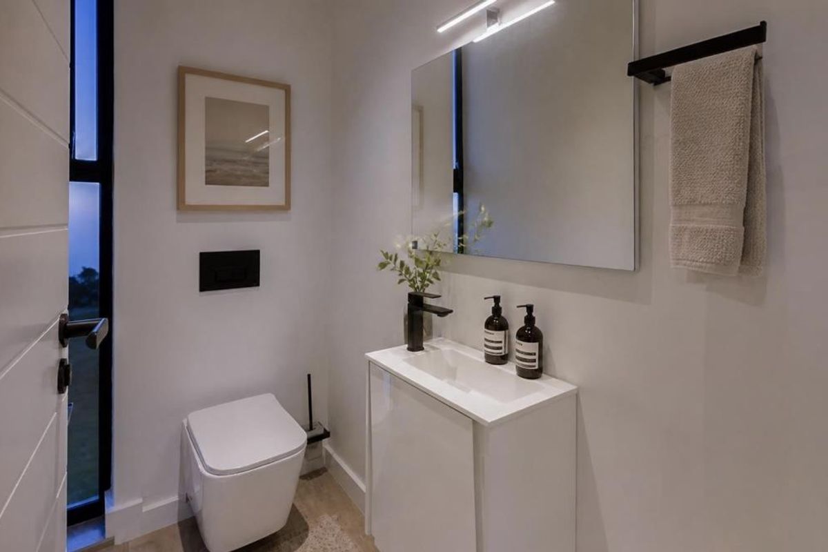 A modern, compact guest bathroom featuring a wall-hung toilet, sleek vanity cabinet with basin, and contemporary black fixtures.