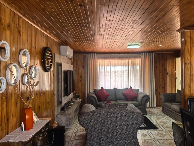 A living room featuring extensive timber wall paneling and a matching wood-clad ceiling, complemented by tiled flooring and a wall-mounted air conditioning unit.