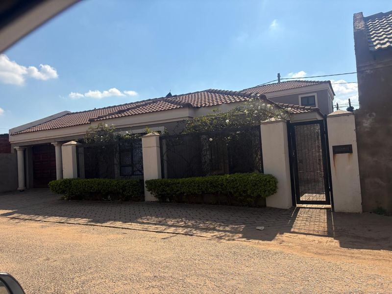 Front exterior view of a single-story house featuring a tiled roof, perimeter wall with metal gate, and a paved driveway.