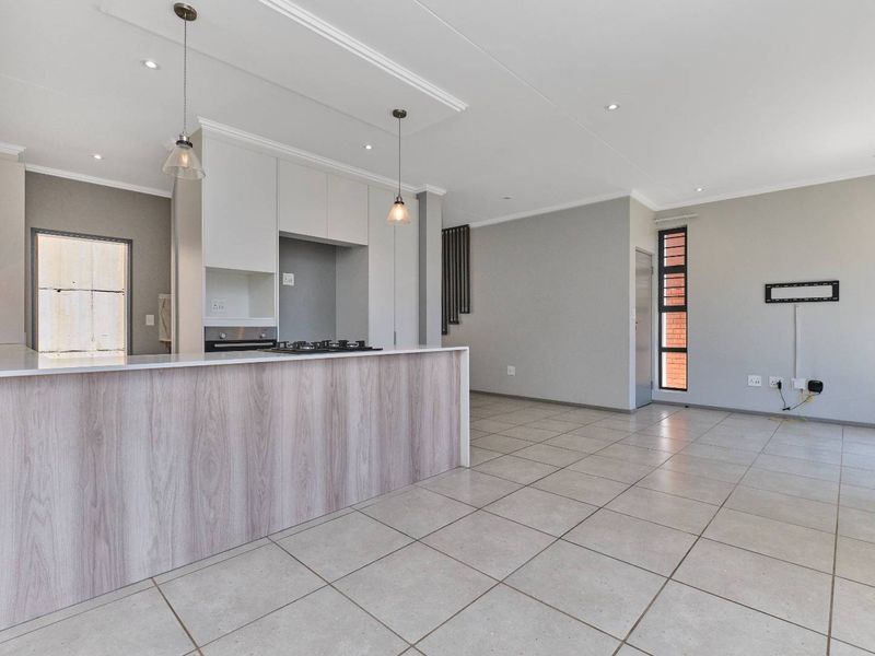 Modern open-plan living area featuring a sleek kitchen with a central island, built-in oven, gas hob, and neutral tiled flooring throughout.