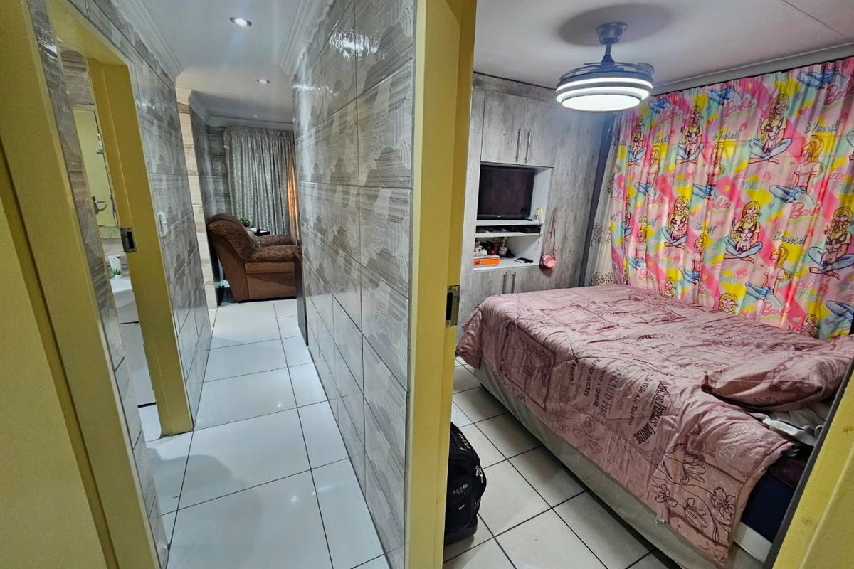 A bedroom featuring tiled walls and flooring, built-in cabinetry, and a ceiling fan, showing signs of dated finishes.