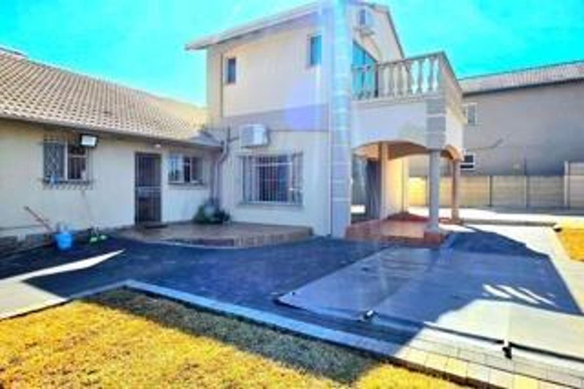 Rear view of a two-story house featuring a paved patio area, a balcony with balustrades, and security bars on the windows.