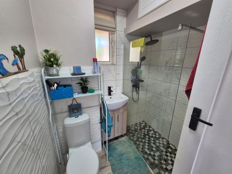 Modern bathroom featuring a walk-in shower with glass screen, vanity basin, toilet, and contemporary textured wall tiling.